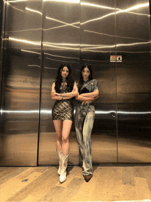 two women standing next to each other in front of an elevator door with a warning sign on it