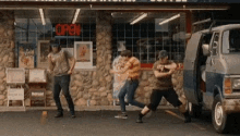 a group of men are dancing in front of a restaurant while a van is parked in front of the restaurant .