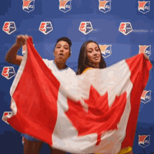 two women holding up a canadian flag in front of a blue wall with shields that say nvvsl on it