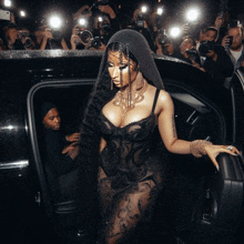 a woman in a black dress is getting out of a car surrounded by photographers