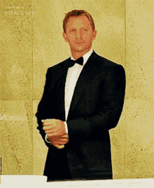 a man in a tuxedo with a bow tie is standing in front of a wall