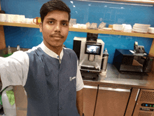 a man taking a selfie in a kitchen wearing a vest that says ' gmtc ' on the front