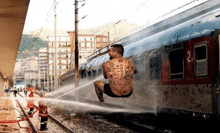 a man with a tattoo on his back is jumping in front of a train that has the number 2 on it