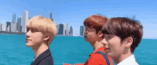 three young men are standing next to each other on a boat in front of a city skyline .