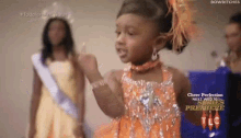 a little girl in an orange dress is giving a thumbs up while standing next to a woman in a yellow dress .