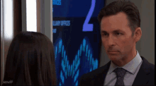 a man in a suit and tie looks at a woman in front of a screen that says ' 2 ' on it