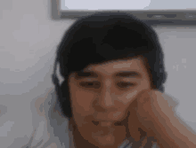 a boy wearing headphones looks at the camera with his hand on his face