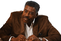 a man in a brown suit is sitting at a desk with his hands folded