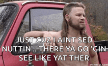 a man with long hair and a mullet is leaning out of a red truck with a cigarette in his mouth .