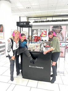 three women are posing in front of a macy 's beauty display