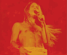 a naked man singing into a microphone with a red background