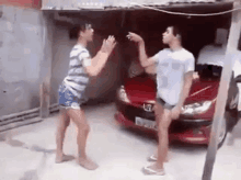 a man and a woman are fighting in front of a red car .