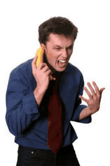 a man in a blue shirt and red tie is holding a banana to his ear while talking on a phone .