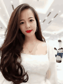 a woman with long hair and red lipstick is wearing a white top and a gold necklace