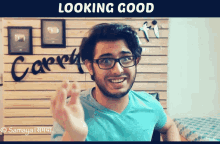 a man wearing glasses is smiling in front of a wall that says looking good