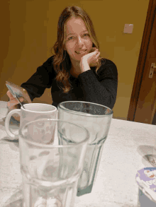 a woman sits at a table with empty glasses and a mug