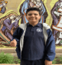 a young boy in a blue jacket is standing in front of a mural of a nativity scene .