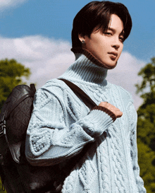 a man wearing a light blue sweater is carrying a backpack