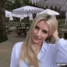 a woman is standing in front of a picnic table with umbrellas in a park .