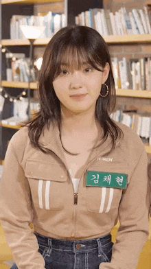 a woman wearing a jacket with a name tag on her chest is standing in front of a bookshelf .