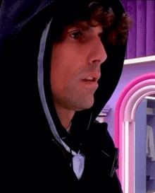 a man with curly hair wearing a black hoodie is standing in front of a mirror .