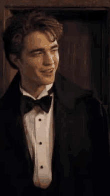 a young man in a tuxedo and bow tie is smiling while standing in front of a door .