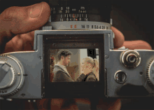 a person is holding a camera with a picture of a man and woman on the screen between the numbers 16 11 and 8