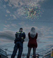 a man and a woman watching fireworks with the man wearing a vest that says " emergency rescue "