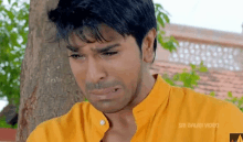 a man in a yellow shirt is sitting under a tree and crying .