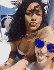 two women are posing for a picture on a boat . one of the women is wearing sunglasses .