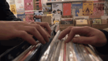 a person 's hands are reaching into a stack of records in front of a wall with posters for pulp fiction