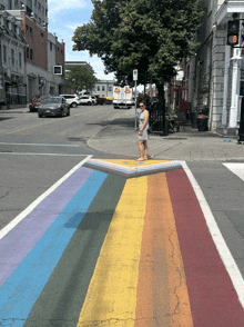 a woman crosses a rainbow painted crosswalk