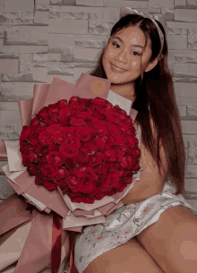 a woman holding a bouquet of red roses in front of a brick wall