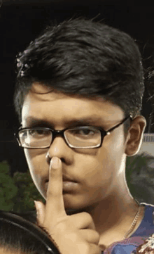 a young boy wearing glasses is pointing at his nose .