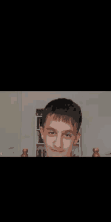 a young boy is making a funny face while sitting in front of a bookshelf in a room .