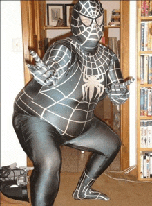 a man in a spiderman costume is squatting down in front of a bookshelf