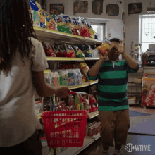 a man in a green and black striped shirt is holding a bag of chips while a woman holds a red basket