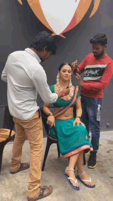 a woman in a green dress is getting her hair done by a man wearing a shirt that says ' krishna ' on it