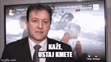 a man in a suit and tie is standing in front of a tv screen that says kaze ustaj kmete