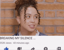 a woman with curly hair is standing in front of a brick wall with a video titled breaking my silence