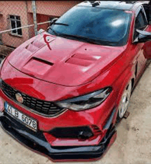 a red car is parked in front of a fence in a parking lot .