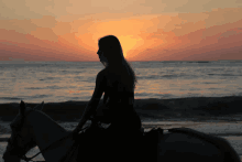 a woman sits on a horse on the beach watching the sunset