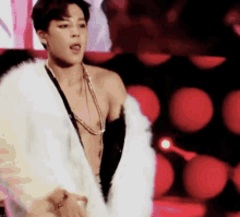 a shirtless man is wearing a white fur coat and a necklace .