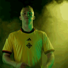 a man in a yellow adidas shirt stands in a dark room