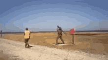 a man in a yellow vest is walking down a dirt road next to a man in a red vest