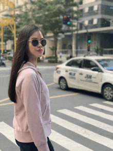 a woman wearing sunglasses is crossing the street in front of a taxi that says jm on the side