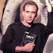 a man in a black sweater holds a copy of dayz