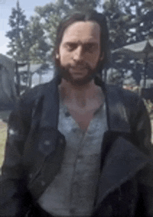 a man with a beard wearing a leather jacket and a white shirt is standing in a field .