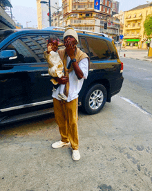 a man holding a baby in front of a black suv