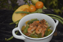 a bowl of shrimp and green beans sits on a table next to vegetables